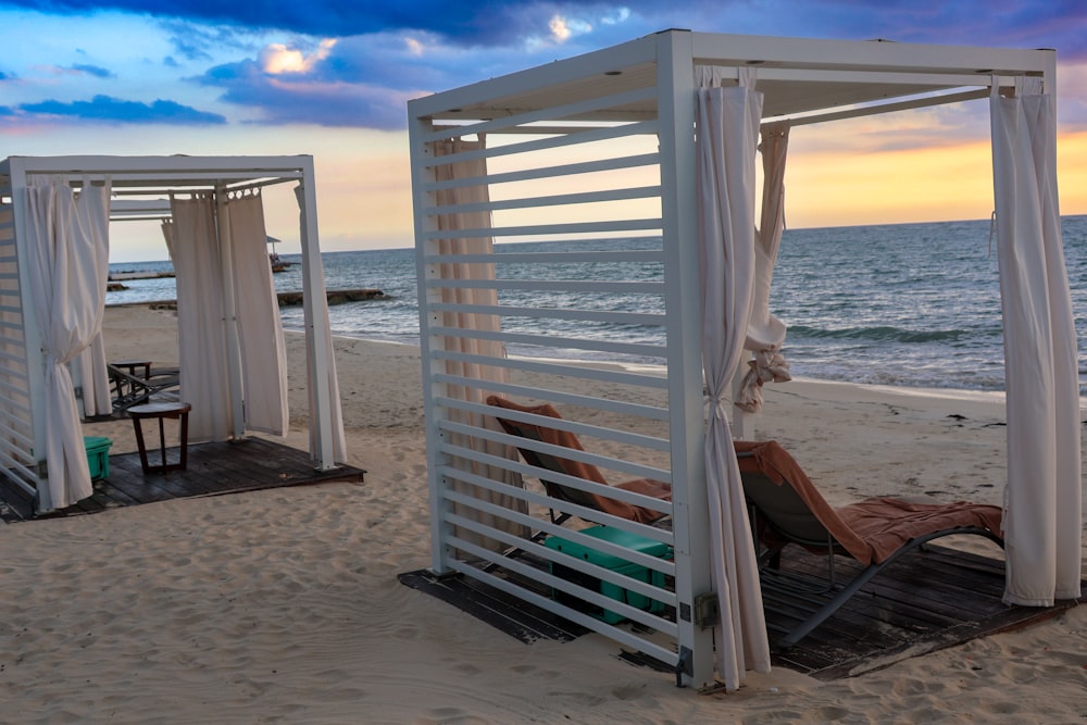 a couple of white cabanas sitting on top of a sandy beach
