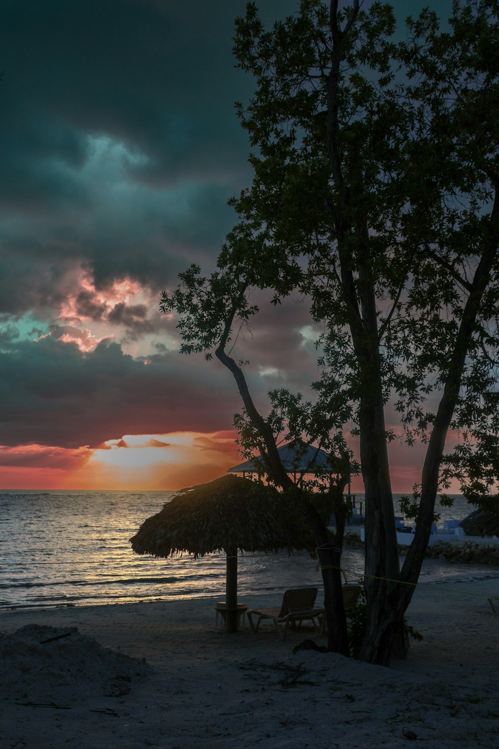 Il sole sta tramontando sulla spiaggia con un ombrellone di paglia
