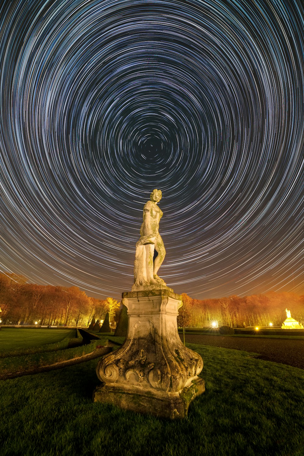 a statue in the middle of a field with a star trail in the background