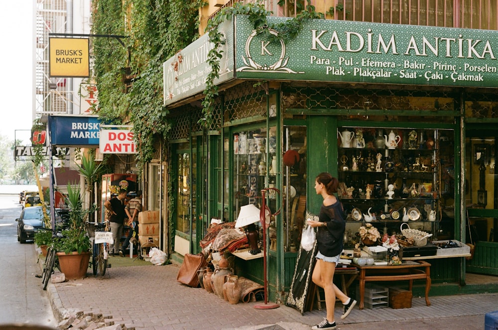 a woman is walking past a shop selling antiques