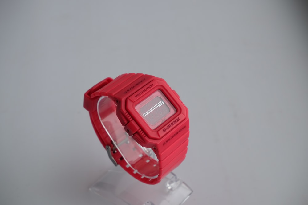 a red watch sitting on top of a clear stand