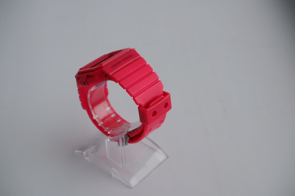a red watch sitting on top of a plastic stand