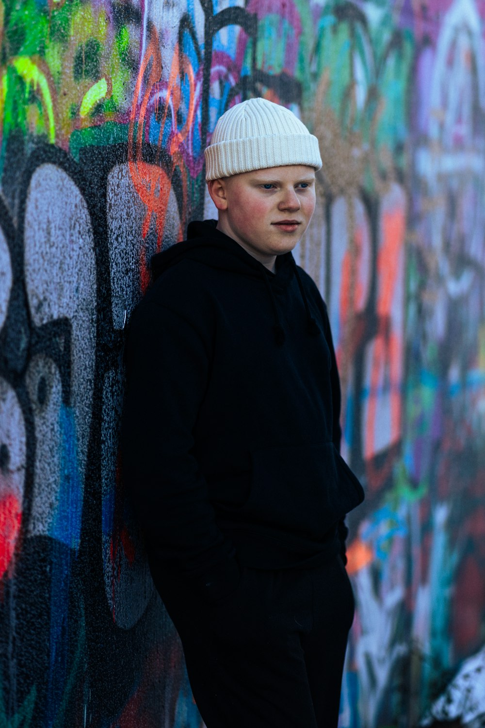a young man leaning against a wall covered in graffiti