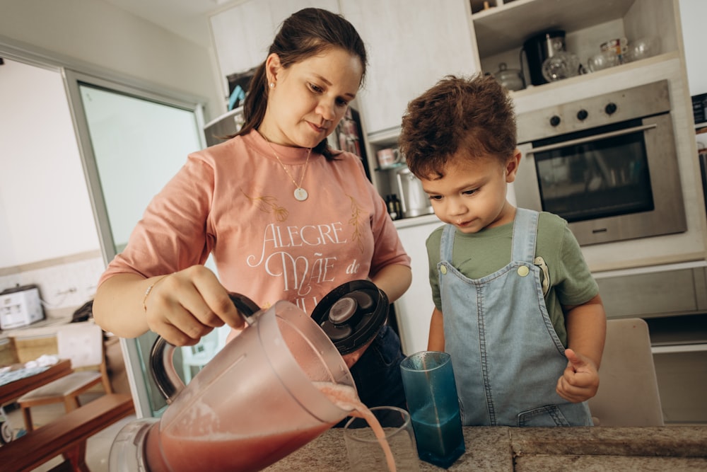 a woman pouring a drink for a boy in a kitchen