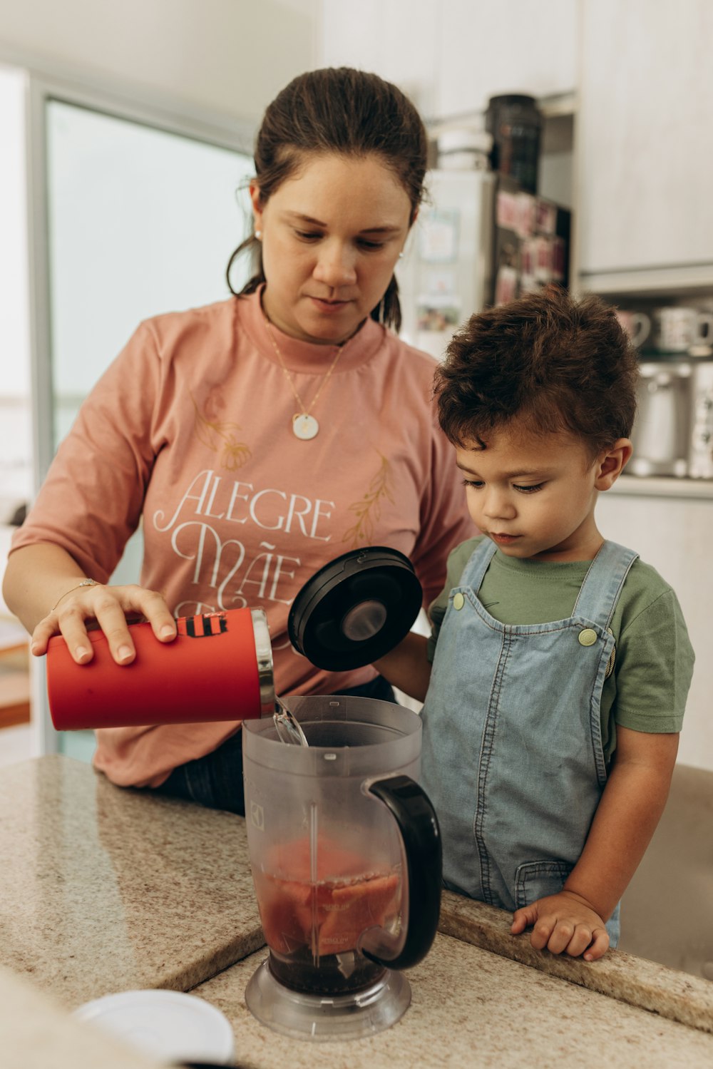 a woman pouring something into a blender with a child