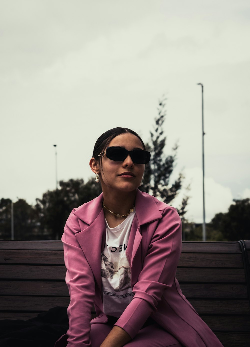une femme en manteau rose et lunettes de soleil assise sur un banc