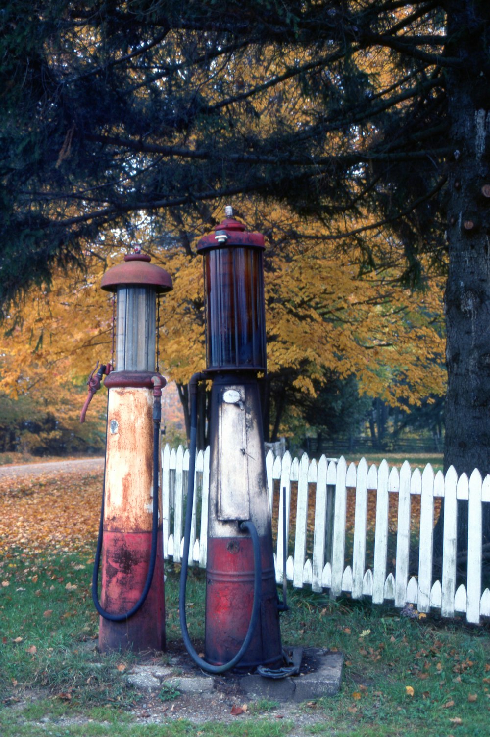 two old fashioned gas pumps in front of a white picket fence