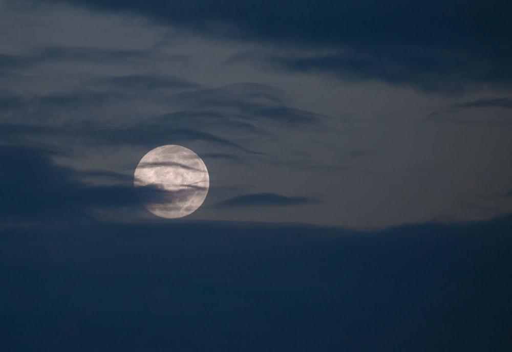a full moon is seen through the clouds