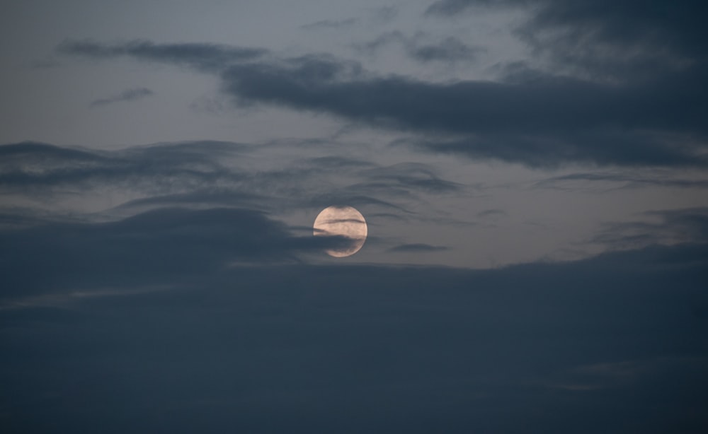 a full moon is seen through a cloudy sky