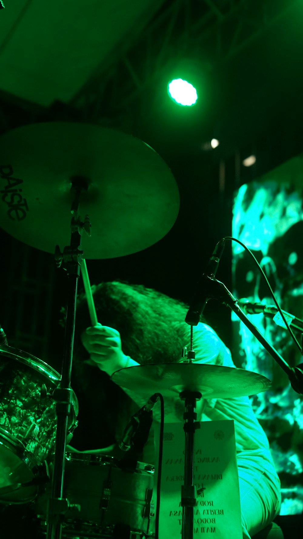 a man playing drums in front of a green light