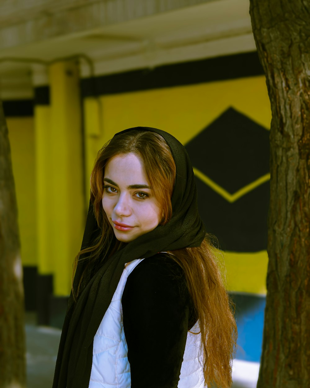 a woman with long red hair standing next to a tree