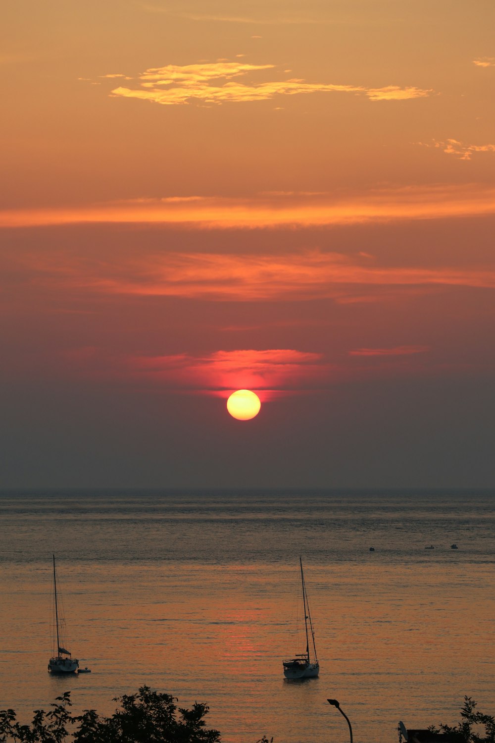 the sun is setting over the ocean with sailboats