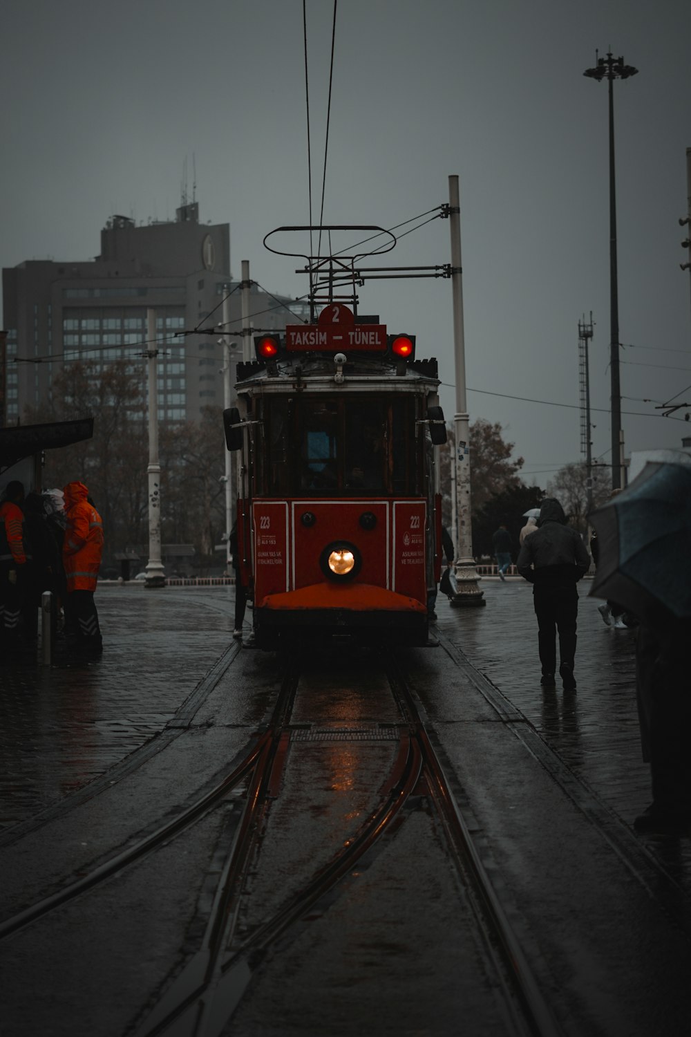 a red trolley car traveling down a rain soaked street