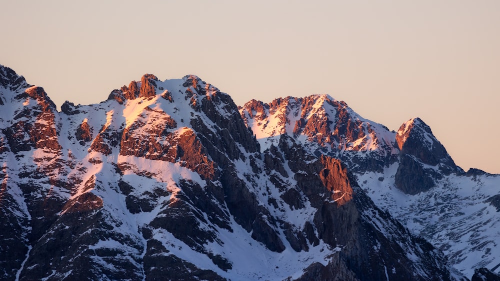 a mountain range covered in snow at sunset