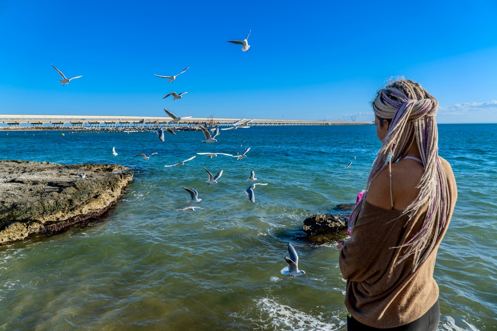 a woman standing in the ocean watching seagulls