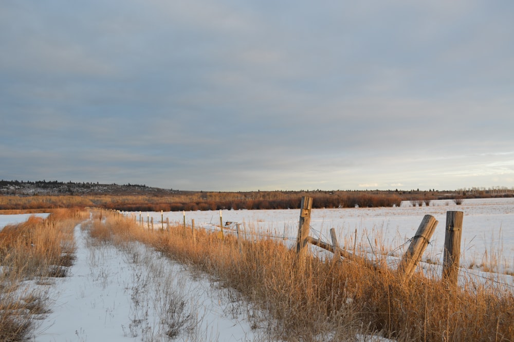 a snow covered field next to a wooden fence