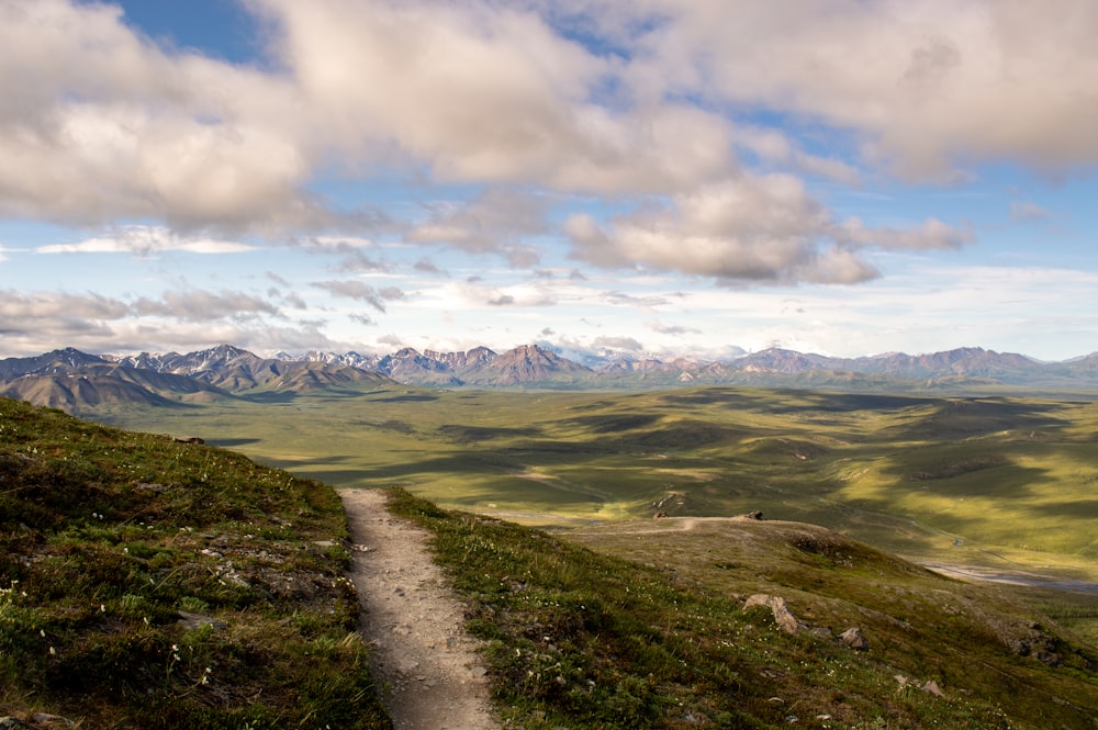 a dirt path on a grassy hill with mountains in the background