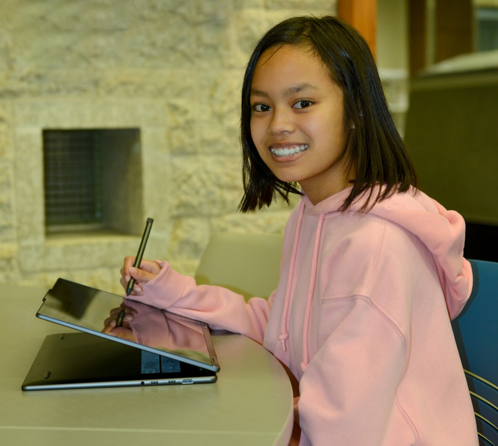 a little girl sitting at a table with a tablet