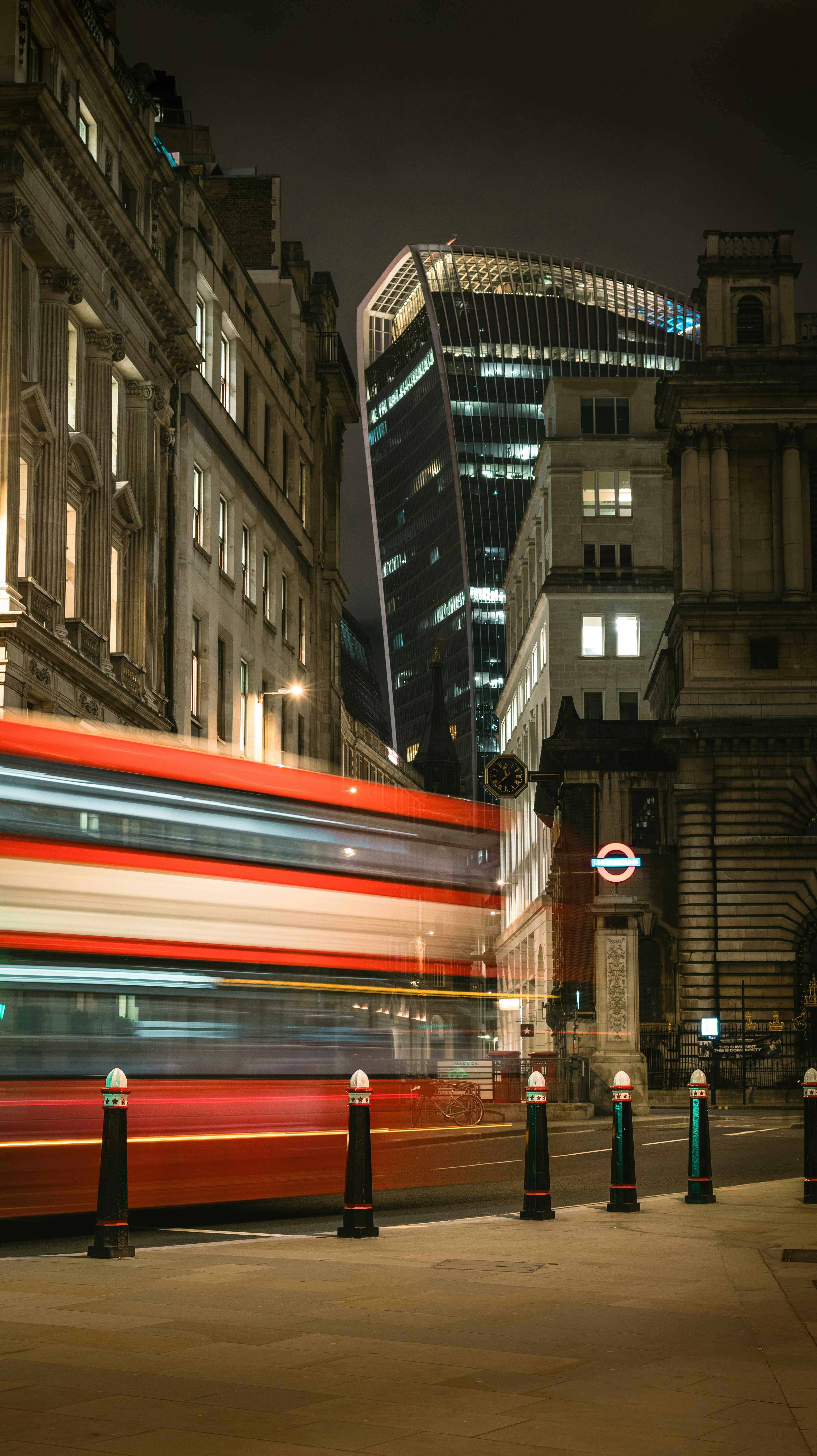 a red double decker bus driving past tall buildings