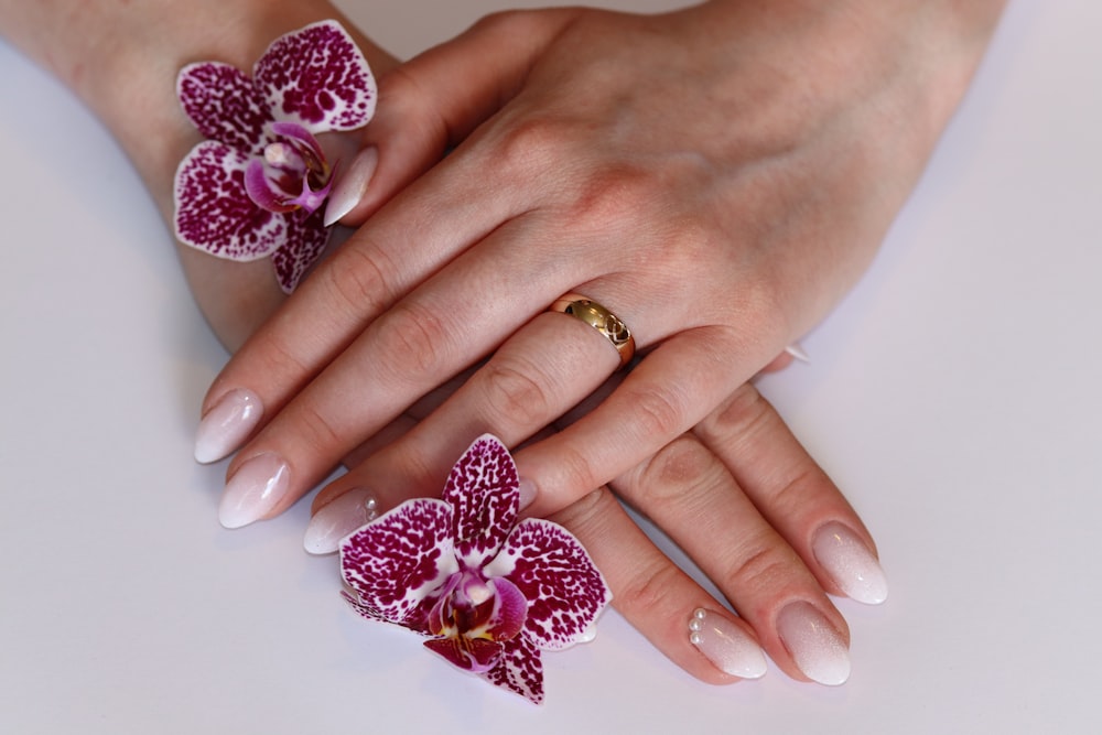 a woman's hand with a ring and two orchids on it