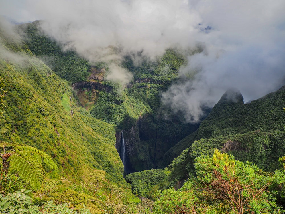 a waterfall surrounded by lush green mountains under a cloudy sky