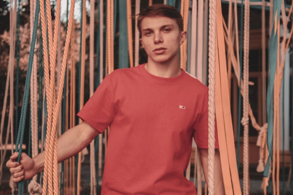 un homme en chemise rouge debout à côté d’un tas de cordes