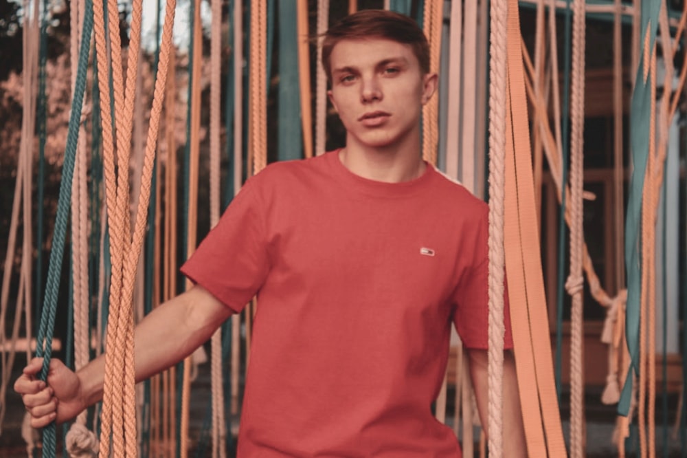 a man in a red shirt standing next to a bunch of ropes