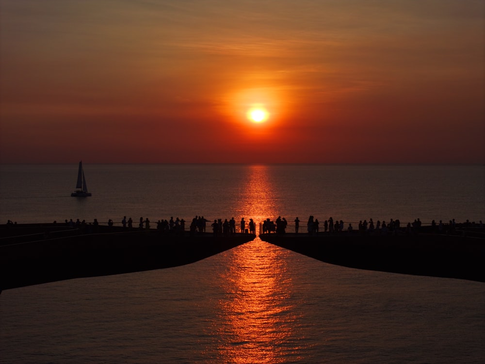 a group of people standing on a pier watching the sun go down