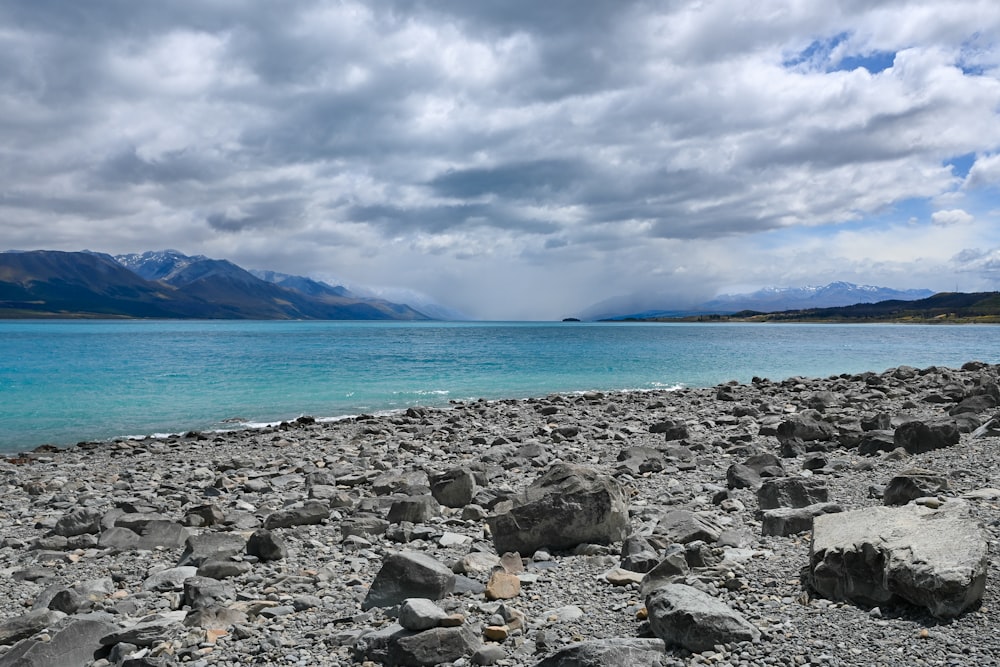 a rocky beach with blue water and mountains in the background