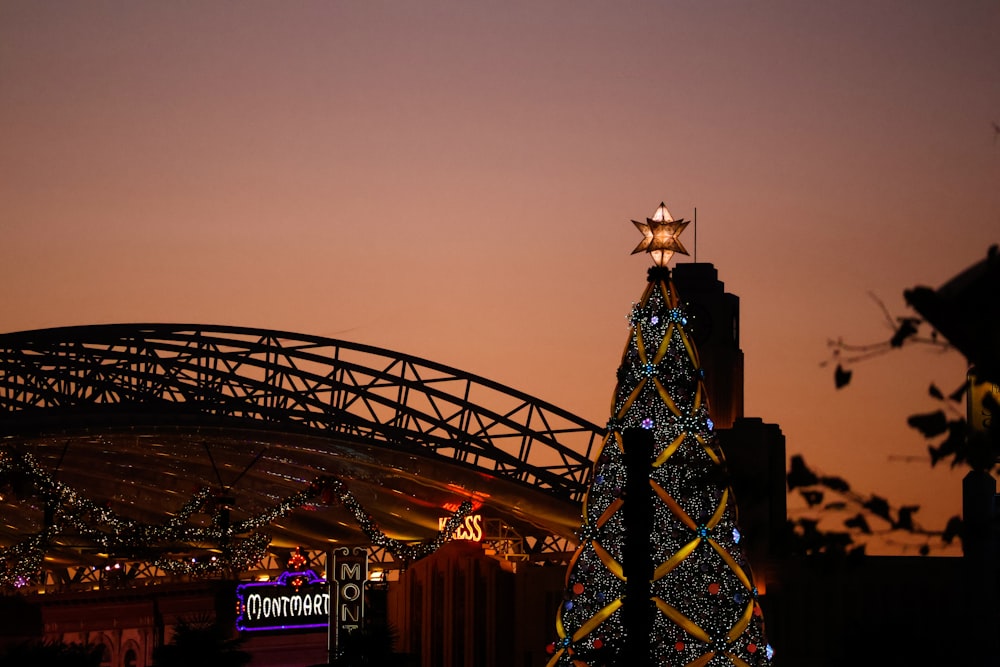 a lit up christmas tree in front of a bridge