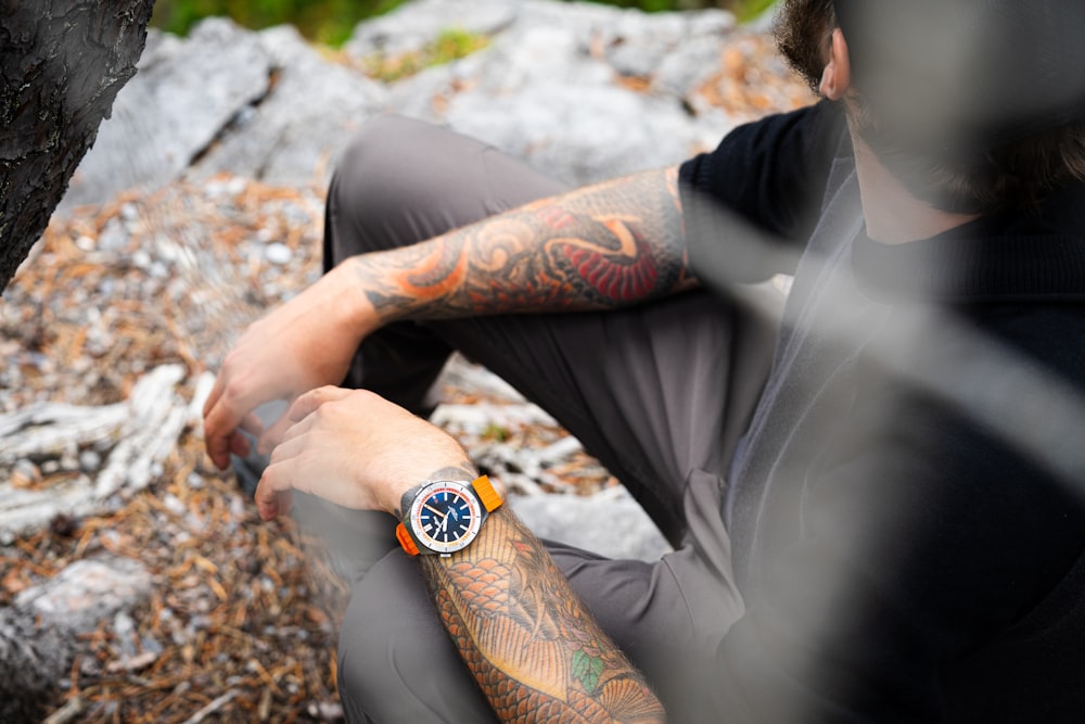 a man sitting on a rock with a tattoo on his arm