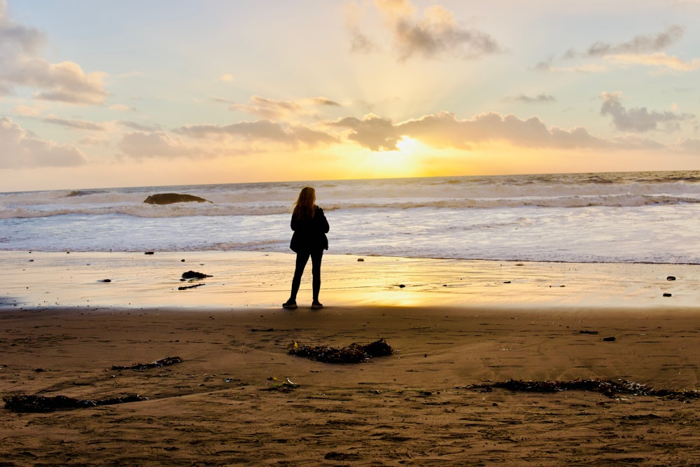 a woman standing on the beach watching the sun go down