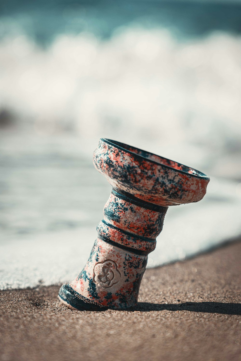 a close up of a vase on a beach near the ocean