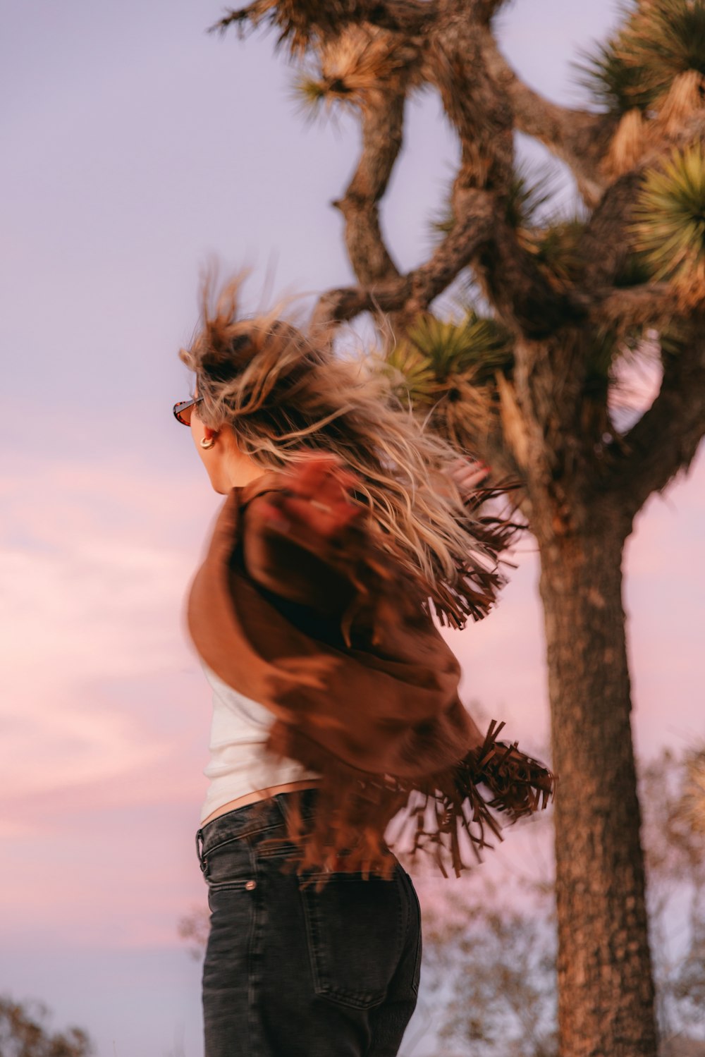 a woman standing in front of a tree with her hair blowing in the wind
