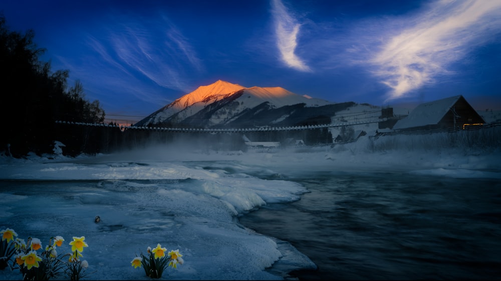 a mountain covered in snow next to a body of water