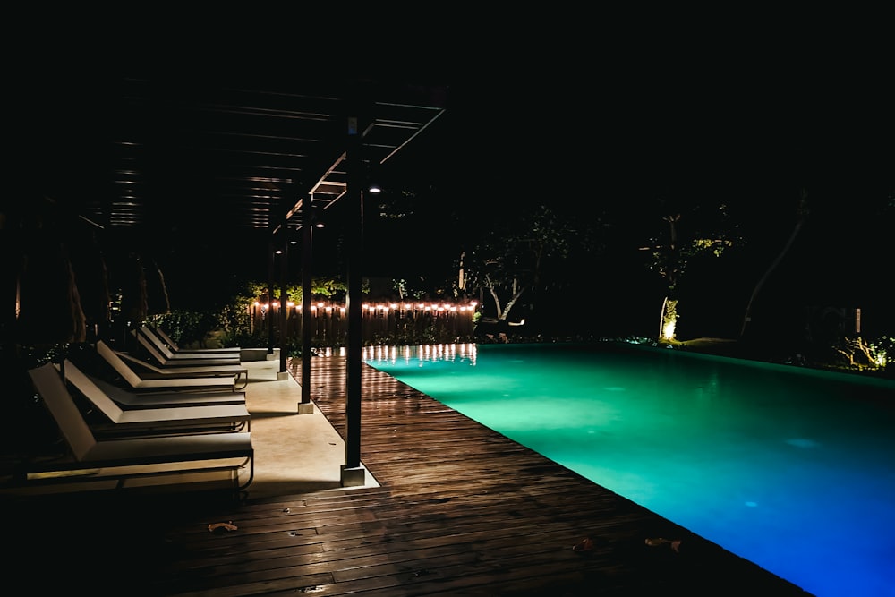 a pool at night with lounge chairs around it