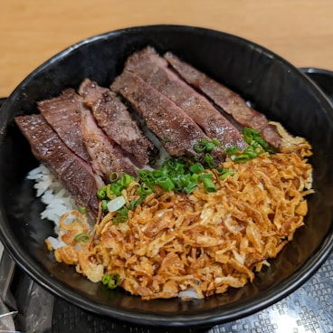 a black bowl filled with meat and rice