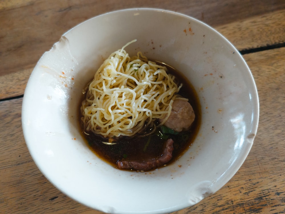 a white bowl filled with noodles and meat