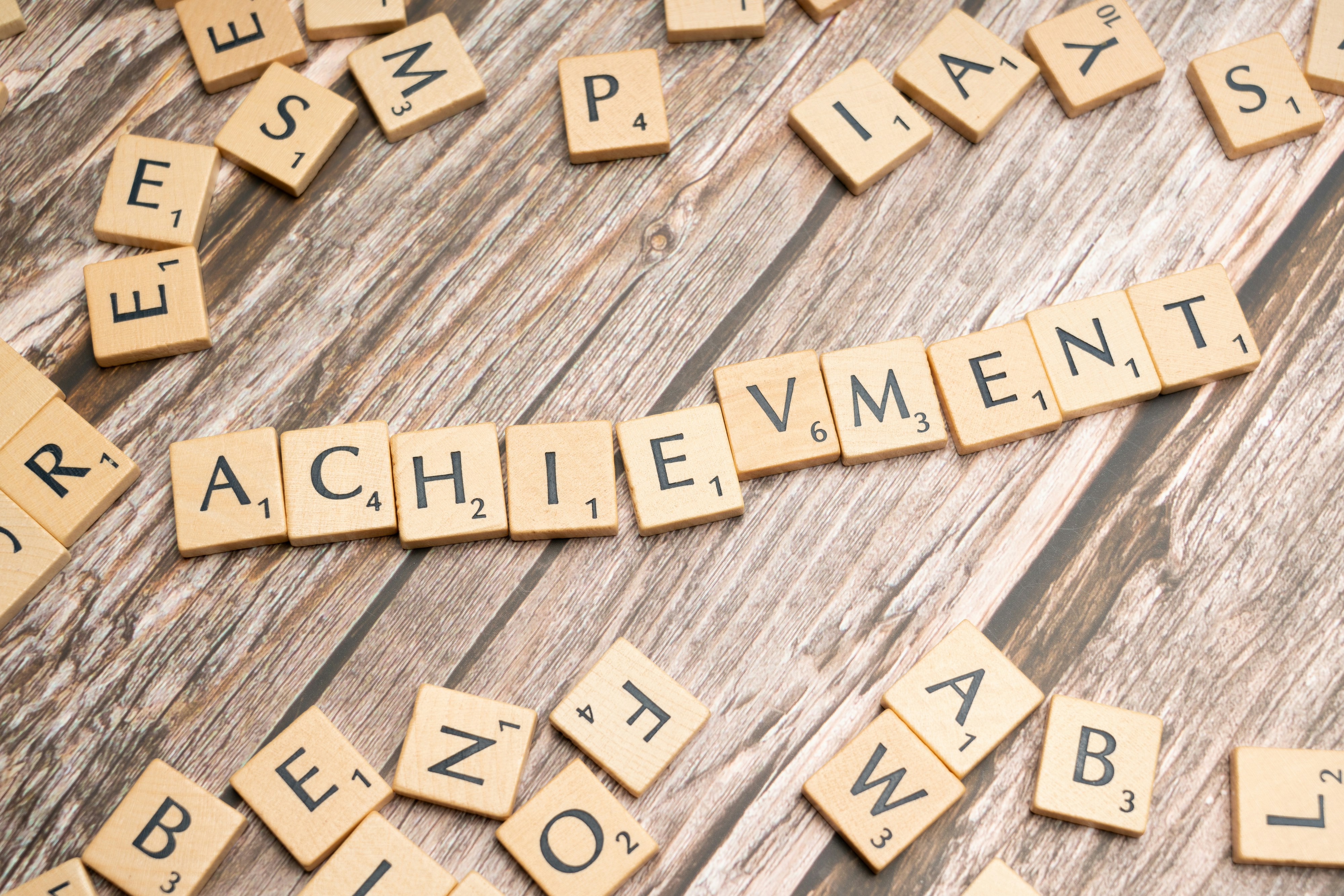 Scrabble tiles spelling "achievement" on wood