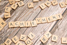 scrabble tiles spelling the word achievement on a wooden surface