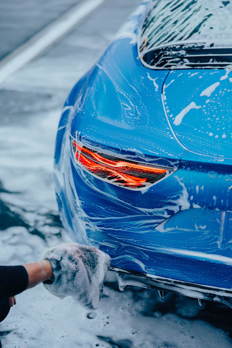 Foam wash suds being rinsed off a blue sports car's rear quarter panel
