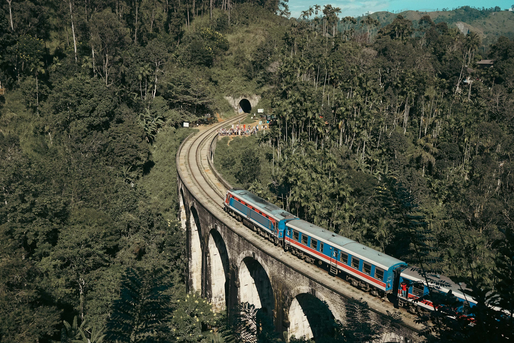 A blue and red train crossing Nine Arches Bridge near Ella