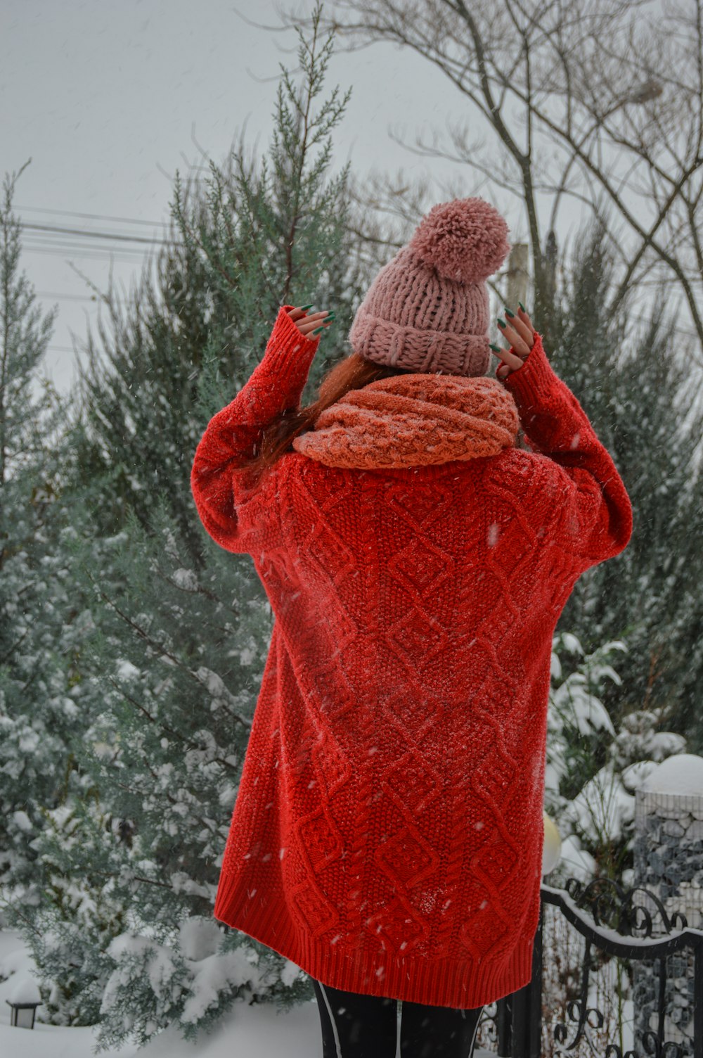a woman in a red sweater and a pink hat standing in the snow