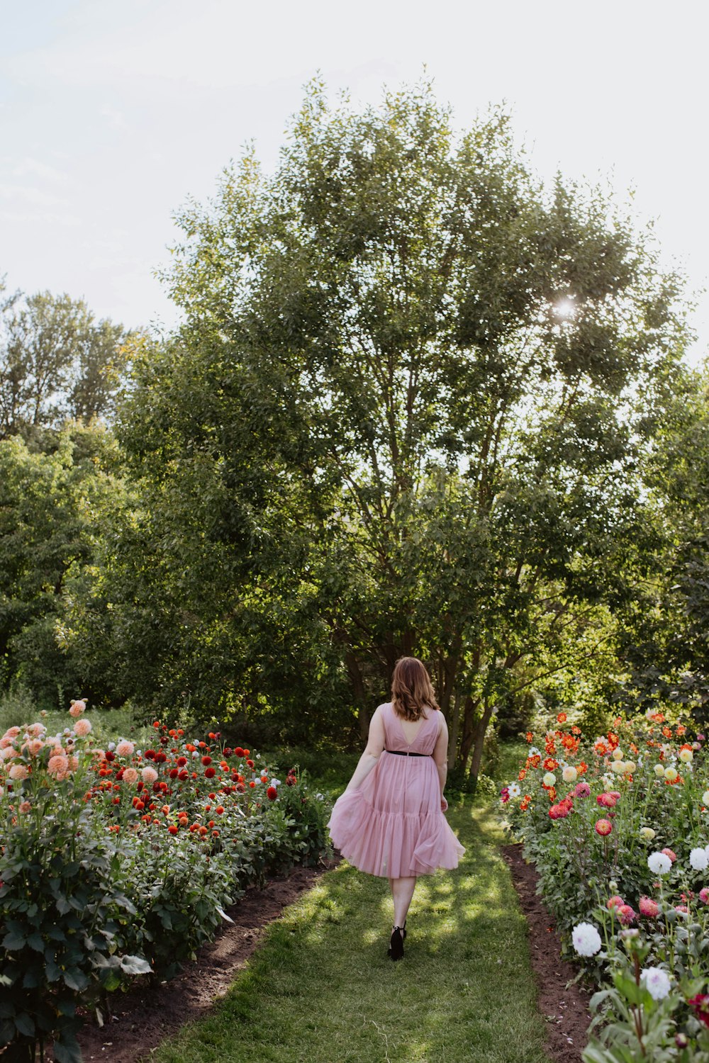 a woman in a pink dress walking through a garden