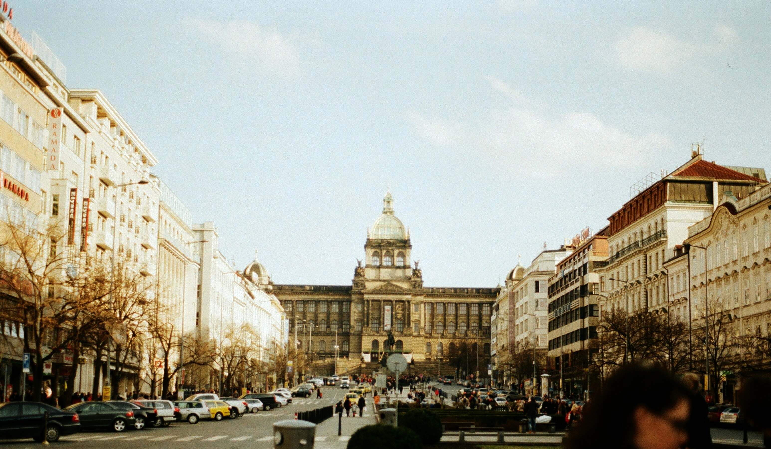 a city street filled with lots of traffic next to tall buildings, The National Museum seen from Vaclavske Namesti.