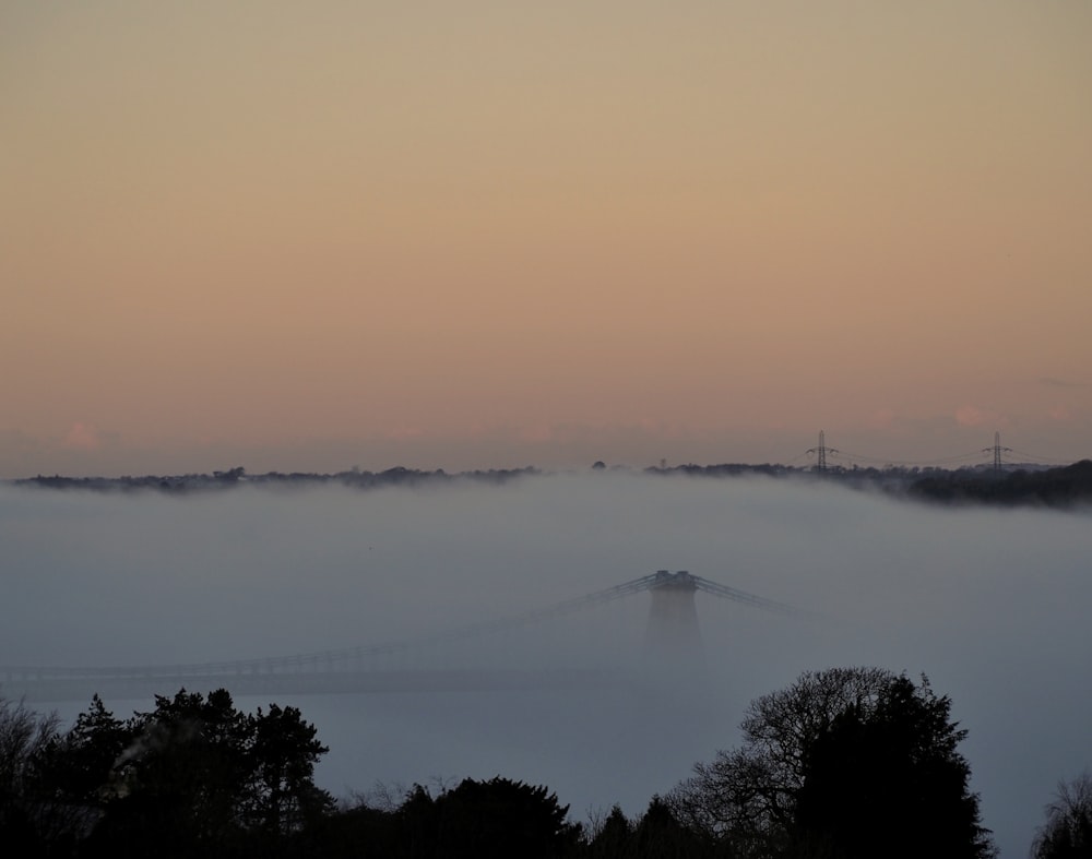 a foggy landscape with a bridge in the distance