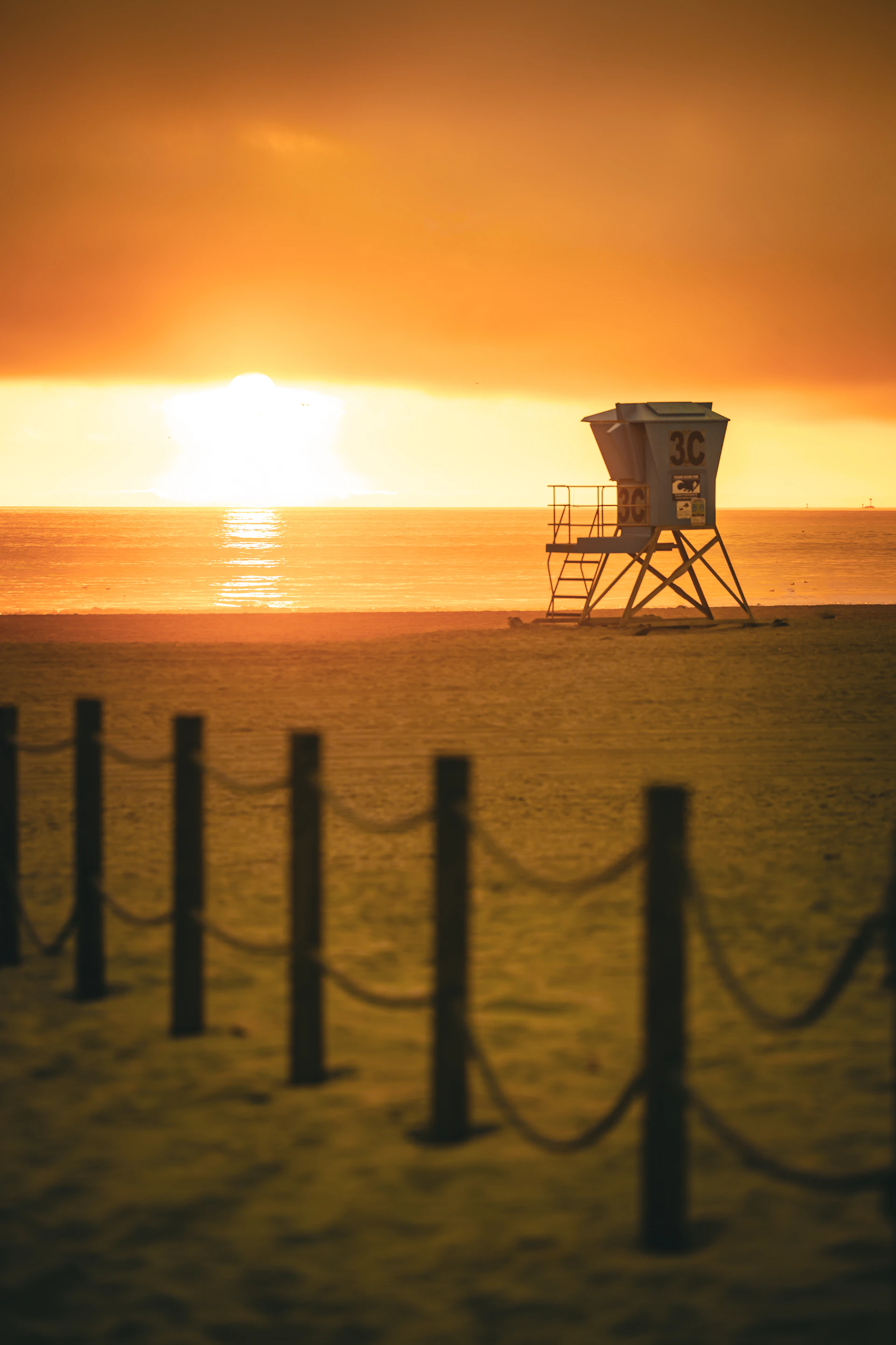 A beach lifeguard stand is lit by the sunset.