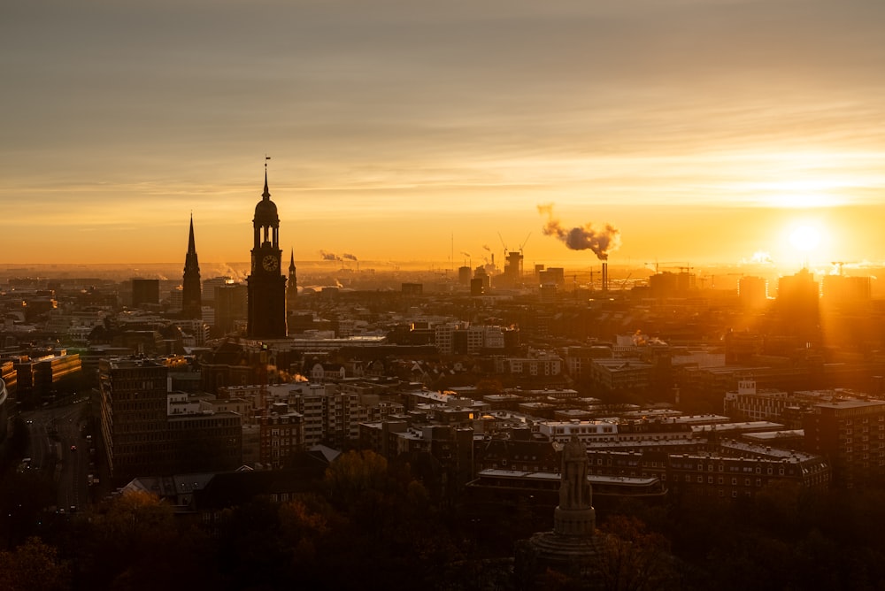 the sun is setting over a city with a clock tower