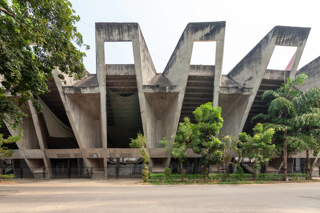 Fasad beton gedung besar dengan barisan pohon di depannya