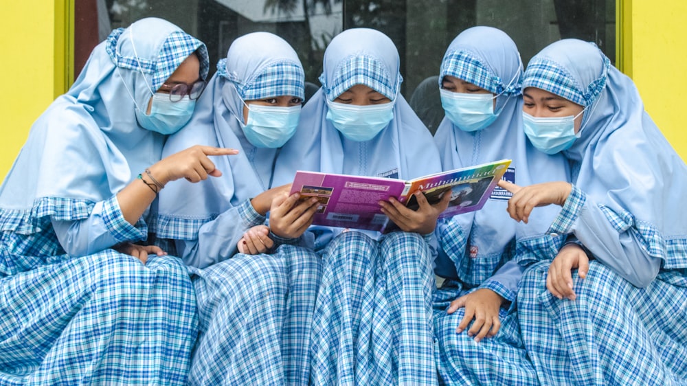 a group of women in blue dresses reading a book